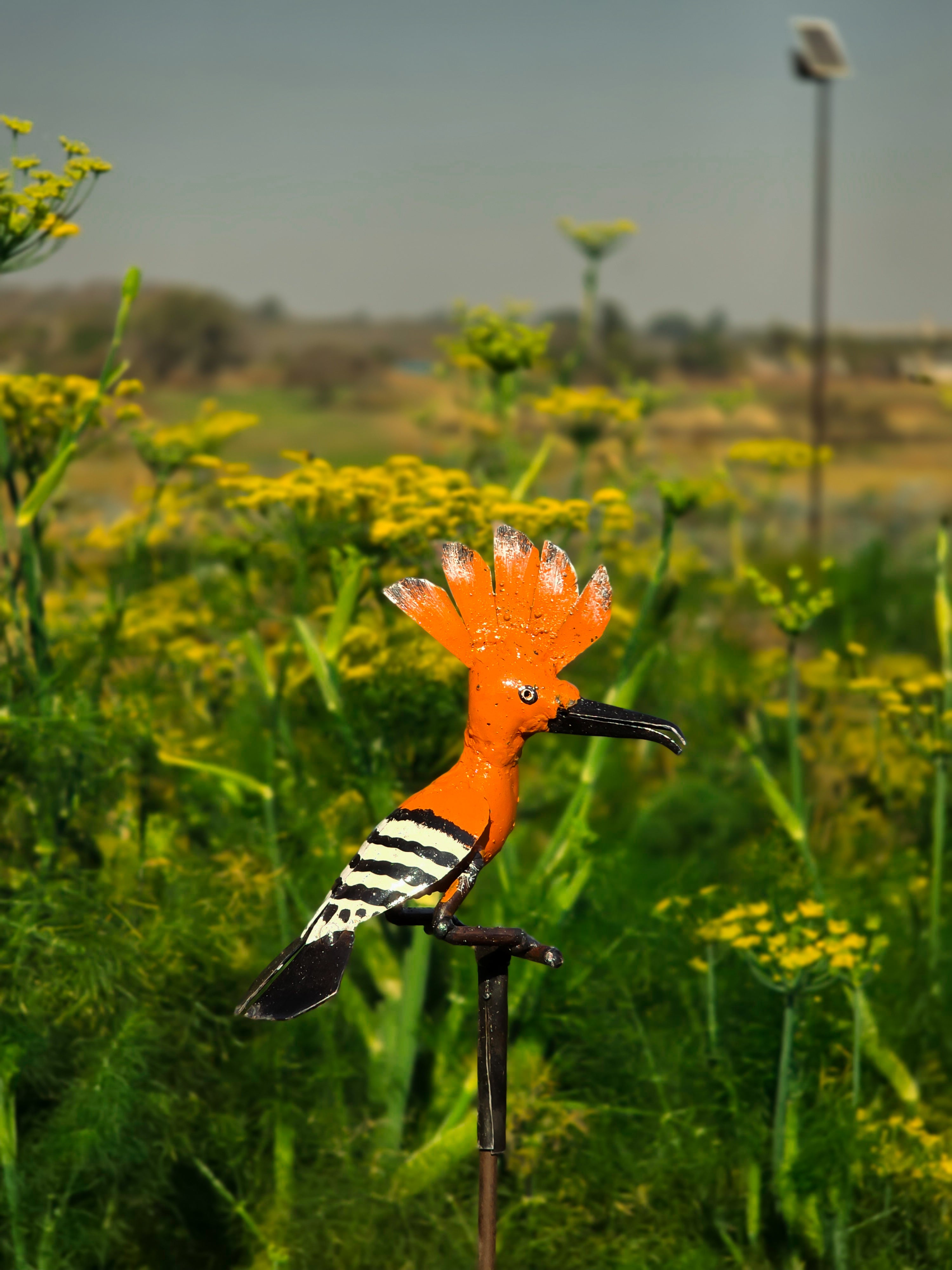Recycled metal hoopoe bird sculpture on rod in flowering garden, weather-resistant Vidaron finish